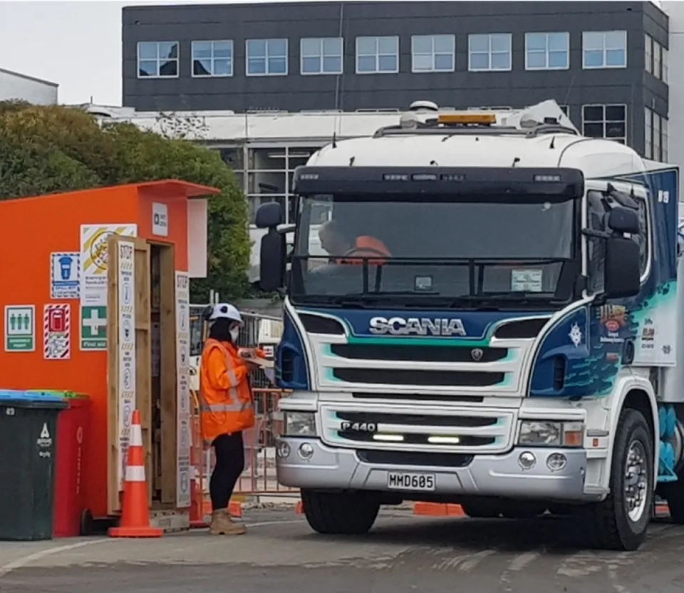 Truck driver speaking with a high-visibility worker at a construction site entrance
