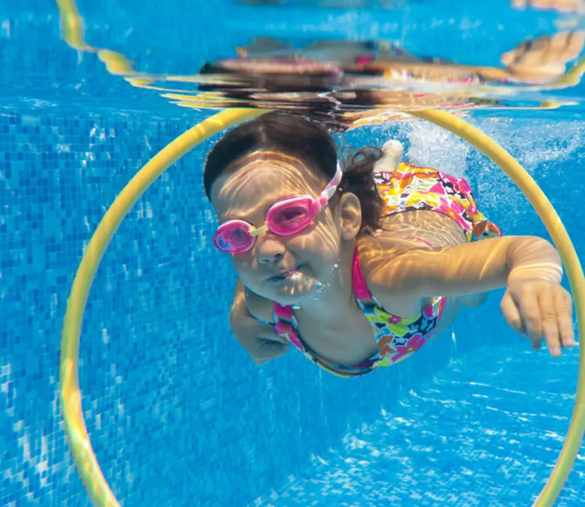 Child wearing pink goggles swimming underwater through a yellow hoop