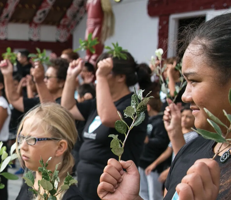 People holding leafy branches at the 2018 Poukai ceremony at Maketu Marae