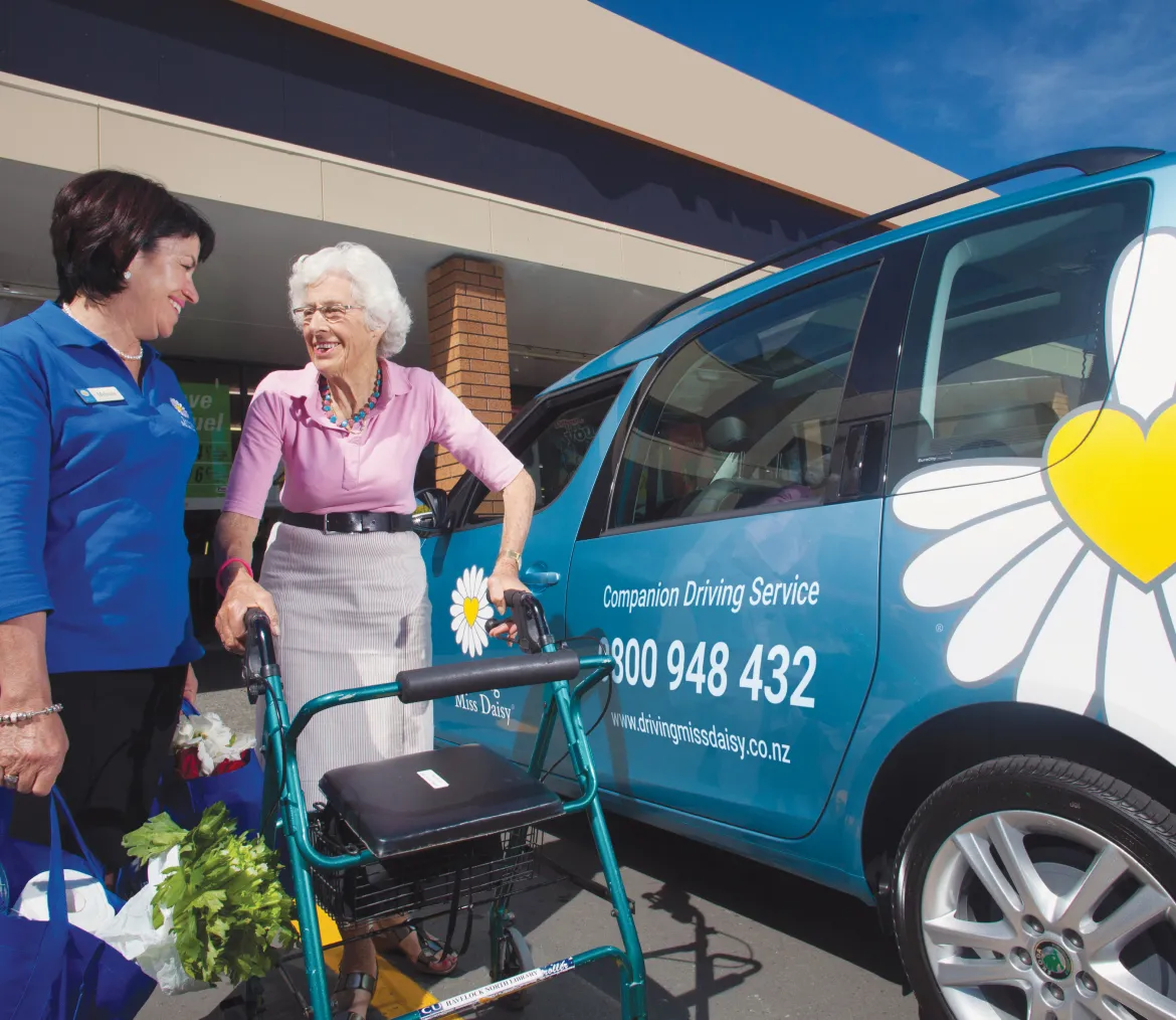 Driving Miss Daisy driver beside a customer using a walking frame and a branded vehicle