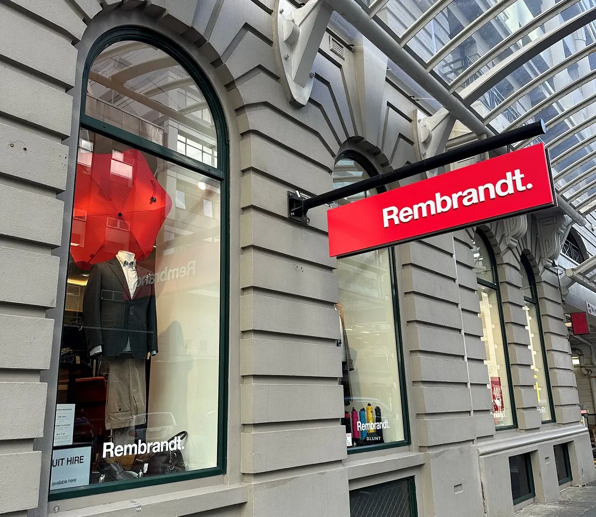 Rembrandt storefront with a red sign and a suit displayed in an arched window