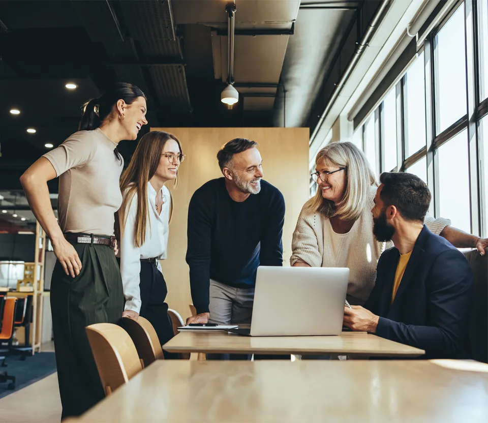 Five people gathered around a laptop at a meeting table